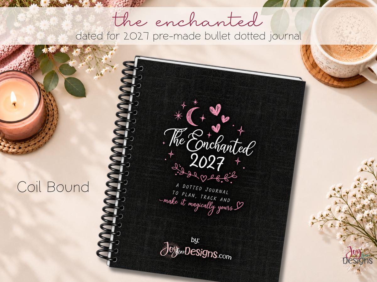 The Enchanted 2027 pre-made dotted journal, an 8 x 10 inch softcover planner with black coil binding and a black linen-look cover decorated with pink hearts, a crescent moon and stars. This dated 2027 journal is designed for creative planning, organization, tracking habits and everyday journaling. A ready-to-use planner with pre-designed pages, monthly themes and space for personal notes, doodles and colouring. Displayed on a desk with flowers and stationery.